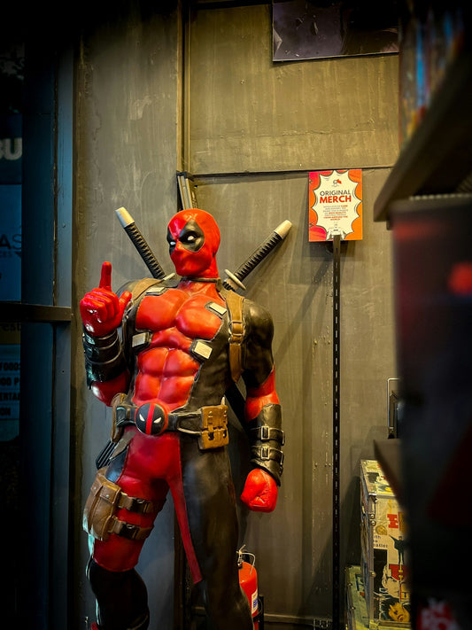 Deadpool statue in black and red costume with swords, displayed in a store corner