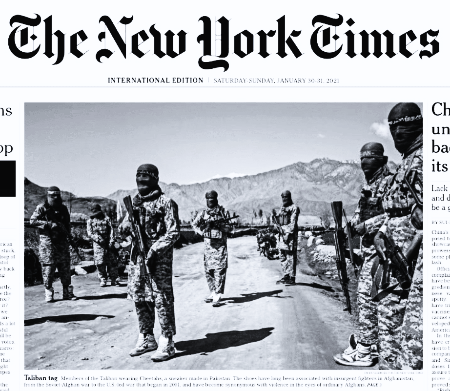 Armed men in camouflage uniforms and face coverings standing on a dirt road with mountains in background, wearing lace-up athletic sneakers.