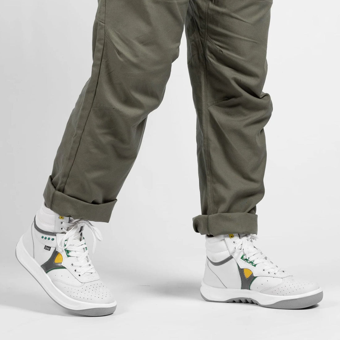 Person wearing white high-top sneakers with green, yellow, and gray accents and khaki pants