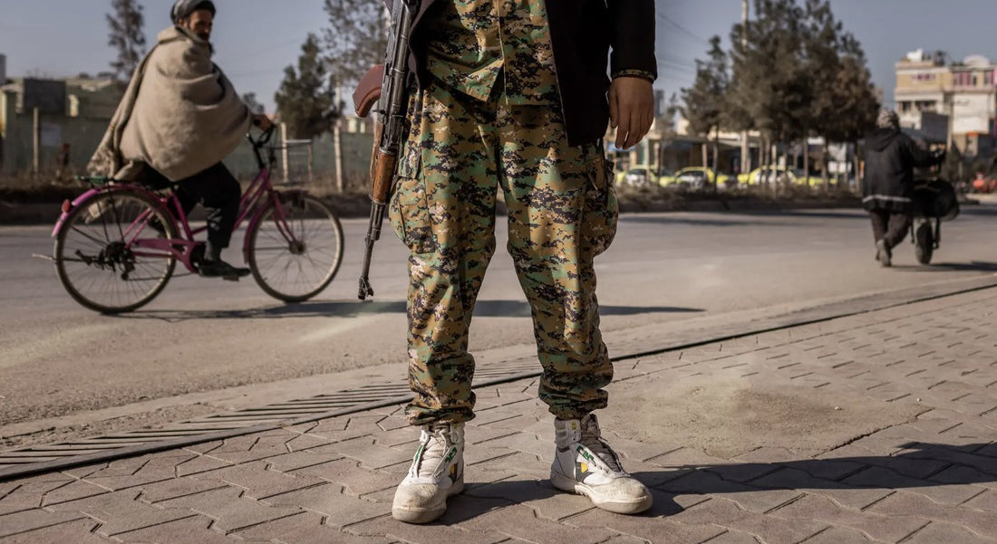Person in camouflage pants and white sneakers standing on sidewalk, street scene in background