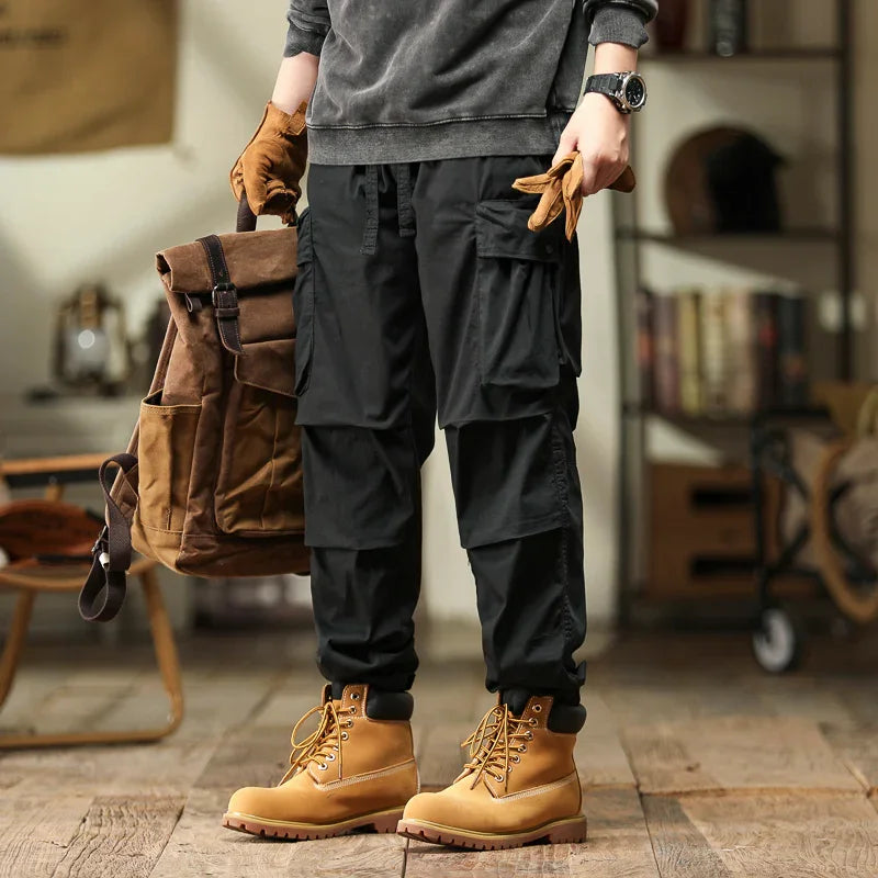 Tan combat boots paired with black cargo pants, brown backpack, and gloves indoors