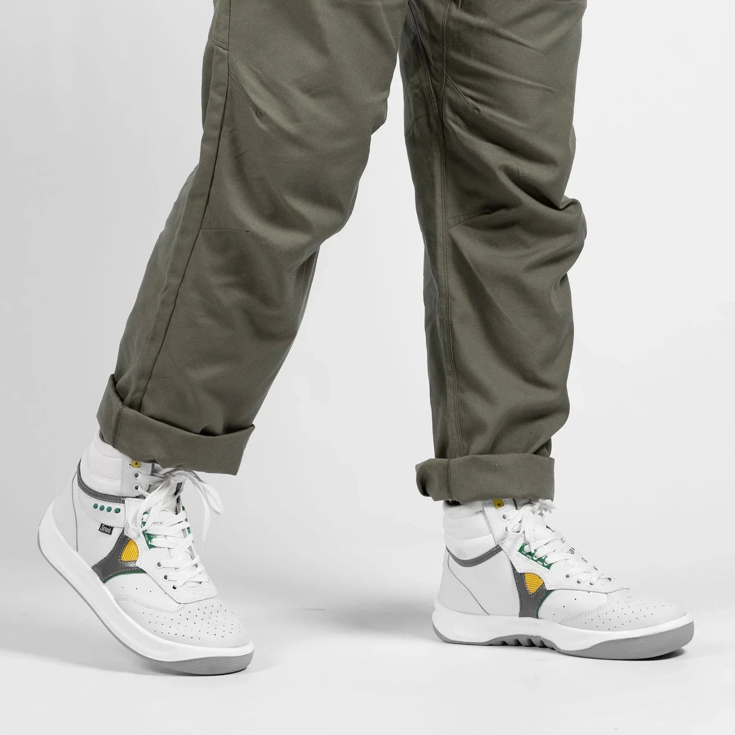 White high-top sneakers with perforated toes, green and yellow accents, worn with rolled-up olive pants.