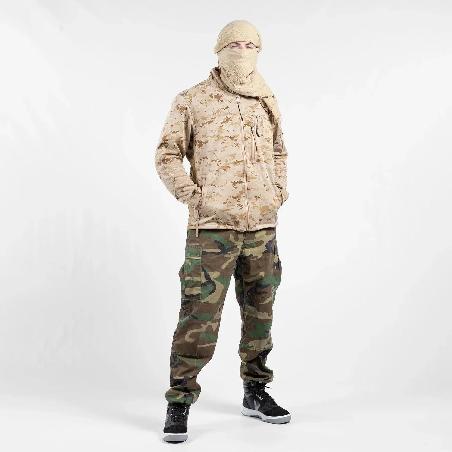 Man in camouflage jacket and cargo pants, face covered, standing on white background