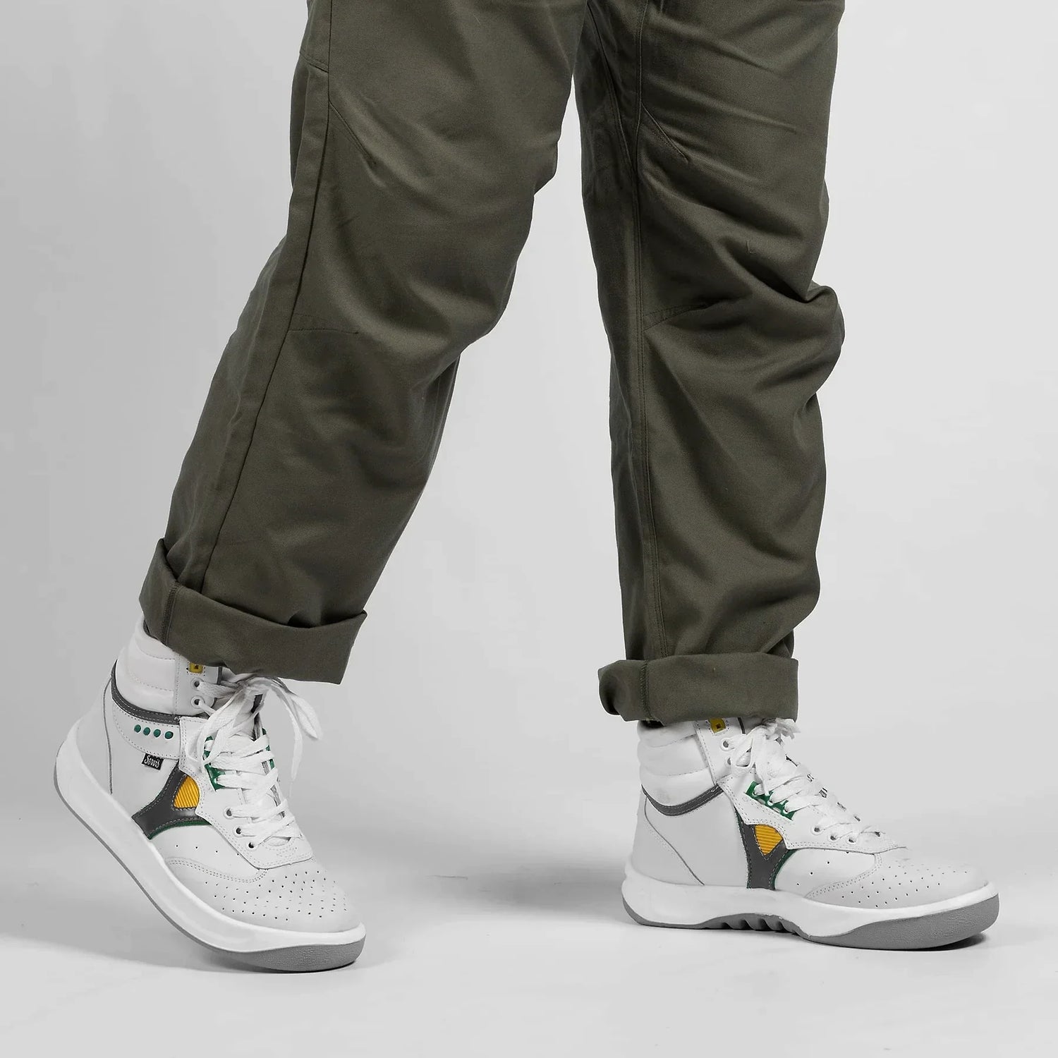 White high-top sneakers with green and yellow accents worn with cuffed olive pants