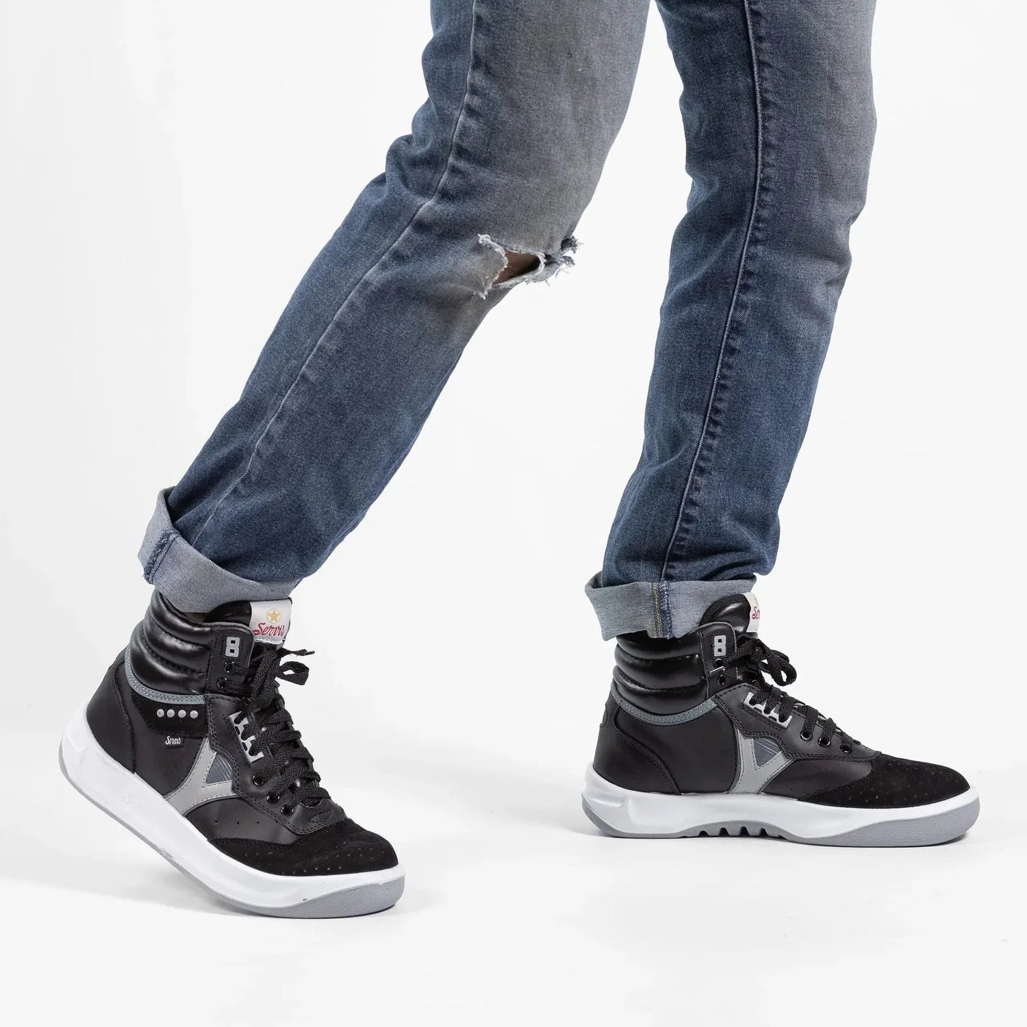 Man wearing black and gray high-top sneakers with jeans on a white background